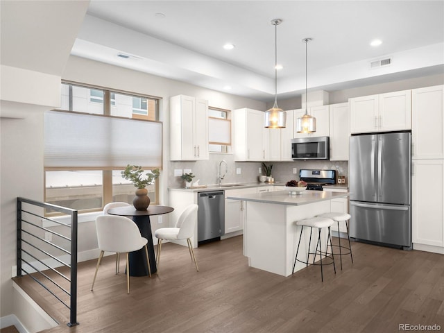 kitchen with sink, appliances with stainless steel finishes, hanging light fixtures, white cabinets, and a kitchen island