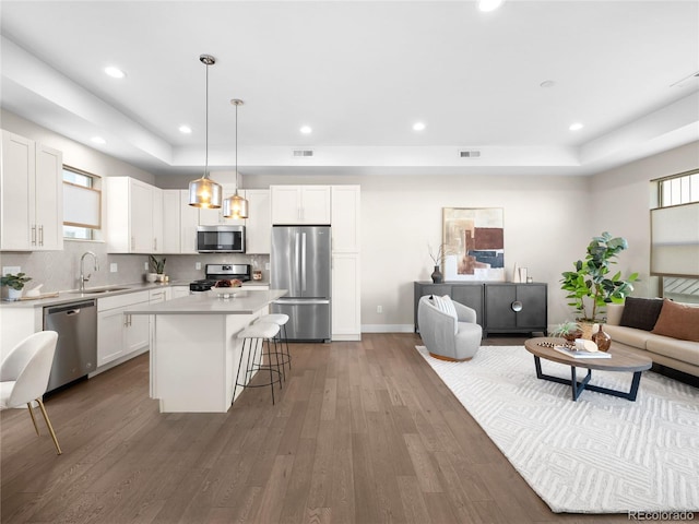 kitchen featuring a tray ceiling, appliances with stainless steel finishes, a sink, and a breakfast bar area