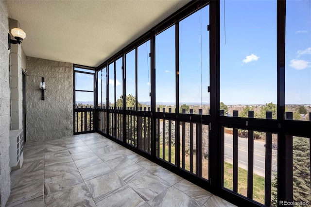 unfurnished sunroom with marble finish floor, a wealth of natural light, expansive windows, and a textured ceiling