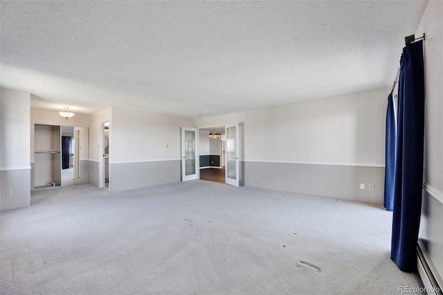 unfurnished living room with a baseboard radiator, a textured ceiling, carpet floors, and an inviting chandelier