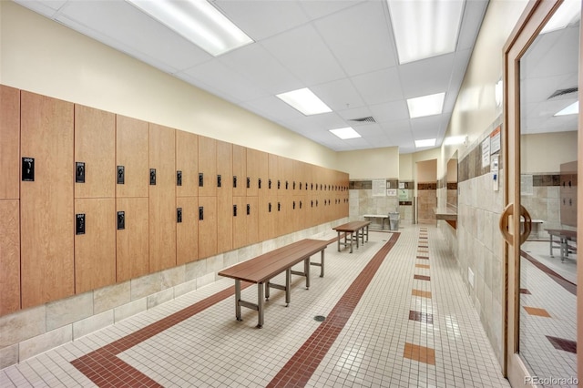 community lobby featuring a paneled ceiling, tile walls, and a wainscoted wall