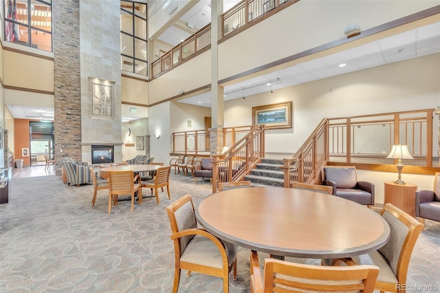 dining room featuring a towering ceiling, stairs, a tile fireplace, and carpet floors