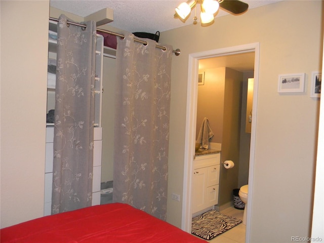 bedroom featuring ensuite bathroom, ceiling fan, light tile patterned flooring, and a textured ceiling