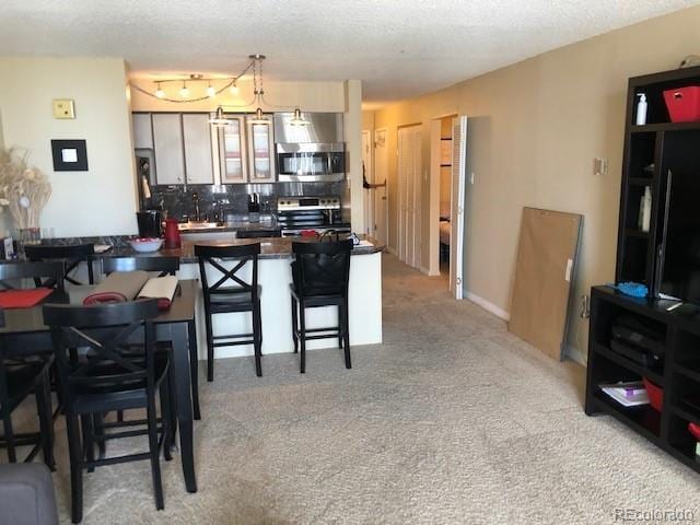 kitchen featuring kitchen peninsula, a kitchen breakfast bar, appliances with stainless steel finishes, a textured ceiling, and light colored carpet