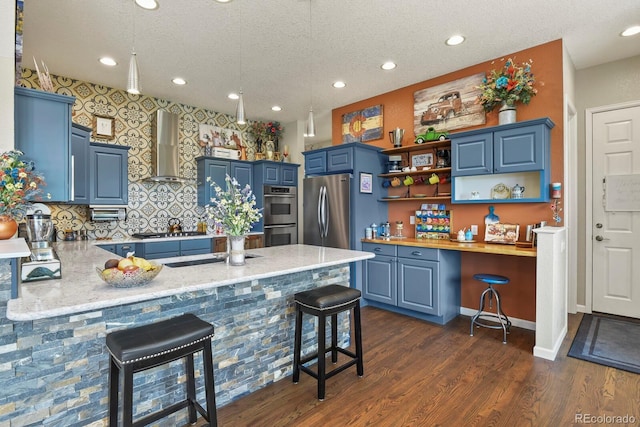 3973 Palmer Ridge Dr, Parker, CO 80134 - kitchen with wall chimney range hood, appliances with stainless steel finishes, blue cabinets, a peninsula, and a textured ceiling