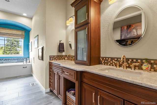3973 Palmer Ridge Dr, Parker, CO 80134 - bathroom featuring double vanity, a textured wall, backsplash, and a bath