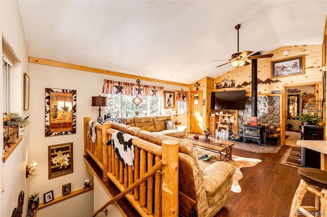 living room with lofted ceiling, a wood stove, dark hardwood / wood-style floors, wooden walls, and ceiling fan