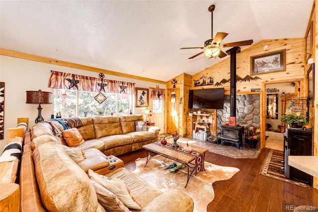 living room featuring dark wood-type flooring, ceiling fan, wood walls, vaulted ceiling, and a wood stove