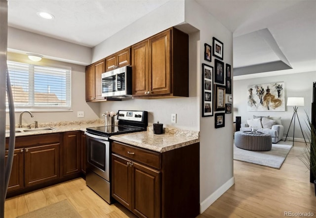 kitchen featuring light stone counters, light wood-type flooring, sink, and appliances with stainless steel finishes