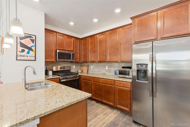 kitchen featuring appliances with stainless steel finishes, light stone counters, sink, light hardwood / wood-style floors, and hanging light fixtures