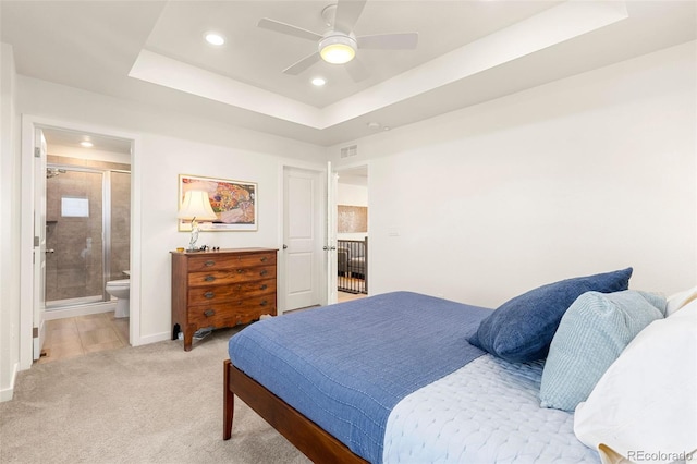 bedroom featuring ceiling fan, light carpet, connected bathroom, and a tray ceiling