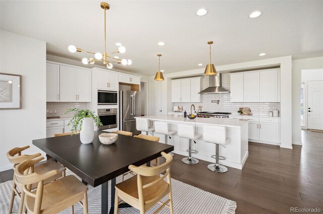 14391 Shasta Daisy Pt, Parker, CO 80134 - kitchen featuring wall chimney range hood, stainless steel appliances, tasteful backsplash, a kitchen island with sink, and recessed lighting