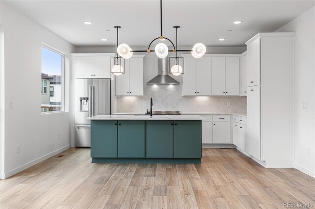 kitchen featuring wall chimney exhaust hood, light hardwood / wood-style floors, tasteful backsplash, high quality fridge, and a healthy amount of sunlight