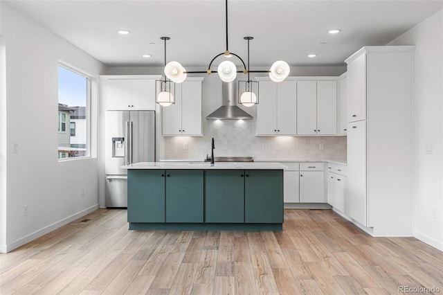 kitchen with high end fridge, wall chimney range hood, pendant lighting, and white cabinets