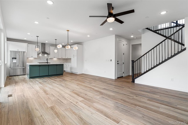 unfurnished living room with sink, ceiling fan with notable chandelier, and light wood-type flooring