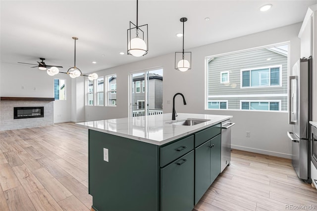 kitchen with ceiling fan, light hardwood / wood-style flooring, a kitchen island with sink, sink, and stainless steel appliances