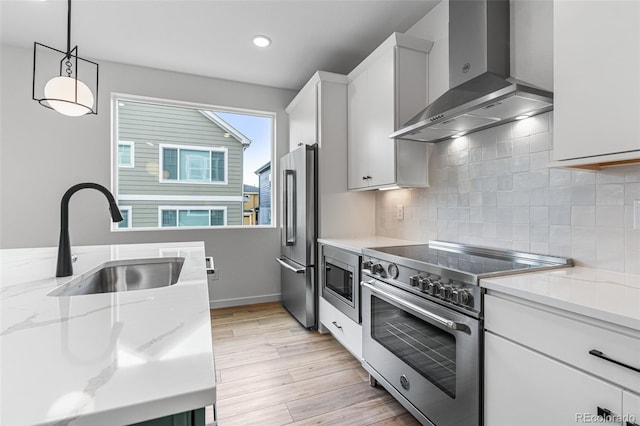 kitchen with decorative light fixtures, light hardwood / wood-style flooring, wall chimney exhaust hood, tasteful backsplash, and high end appliances