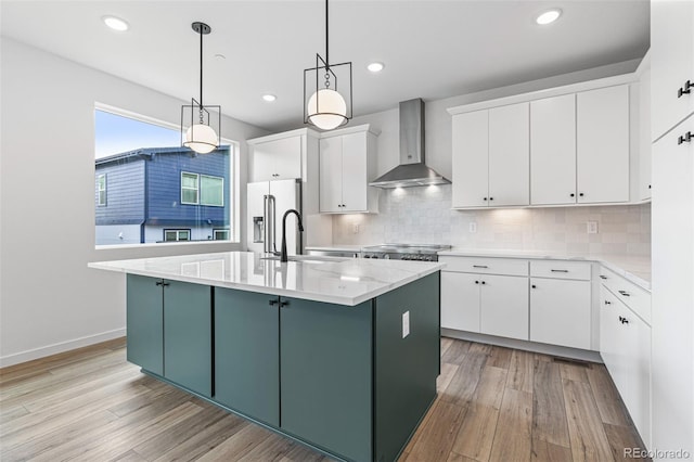 kitchen with light wood-type flooring, appliances with stainless steel finishes, wall chimney exhaust hood, an island with sink, and tasteful backsplash