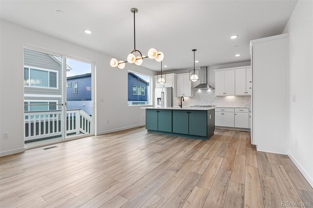 kitchen with high quality fridge, wall chimney exhaust hood, a healthy amount of sunlight, and an island with sink