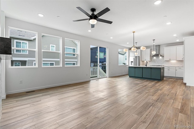 kitchen with white cabinetry, light wood-type flooring, decorative backsplash, stainless steel fridge with ice dispenser, and a center island with sink