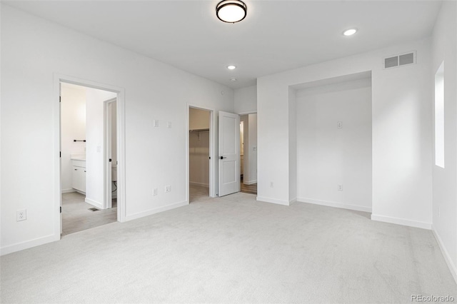 unfurnished bedroom featuring a walk in closet, light colored carpet, a closet, and ensuite bath