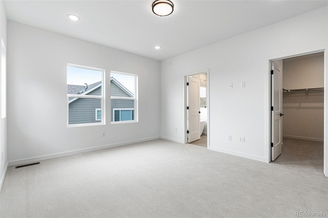 unfurnished bedroom featuring a walk in closet, a closet, ensuite bath, and light carpet