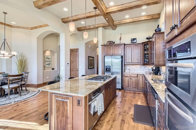 kitchen with a center island, backsplash, hanging light fixtures, light hardwood / wood-style flooring, and stainless steel appliances