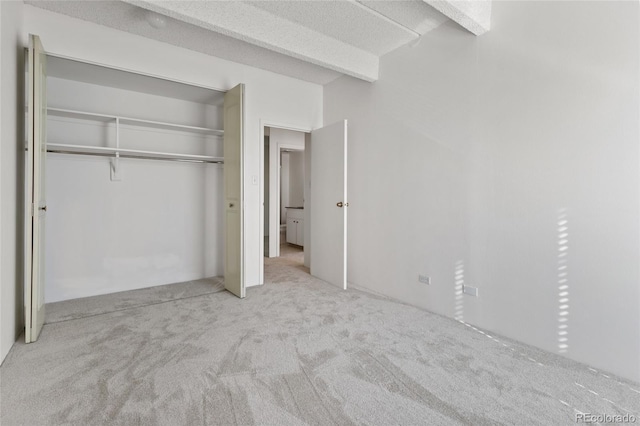 unfurnished bedroom with a closet, beam ceiling, and light carpet