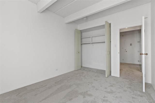 unfurnished bedroom featuring beamed ceiling, a closet, and light carpet