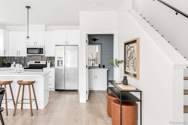 3955 W 13th Ave, Denver, CO 80204 - kitchen featuring stainless steel appliances, a breakfast bar, light wood-type flooring, white cabinetry, and recessed lighting