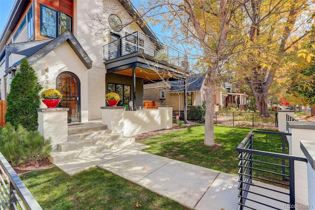 view of front of property featuring brick siding, fence, a porch, a front yard, and a balcony