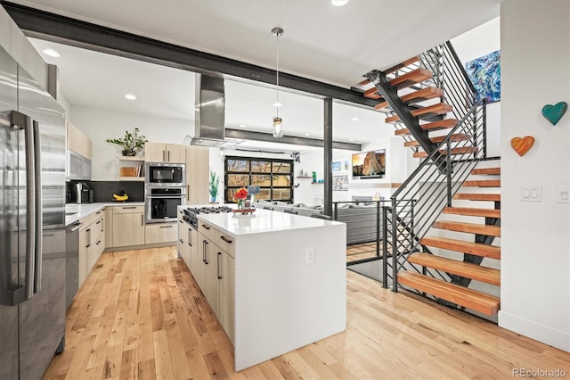 kitchen with light wood finished floors, a center island, light countertops, appliances with stainless steel finishes, and wall chimney exhaust hood