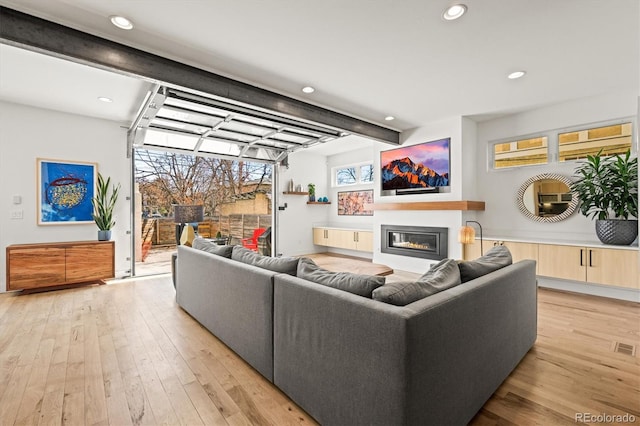 living room featuring a glass covered fireplace, beamed ceiling, recessed lighting, and light wood-type flooring