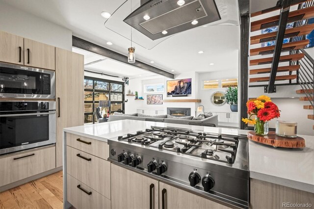 kitchen with a glass covered fireplace, stainless steel appliances, light wood finished floors, and light brown cabinetry