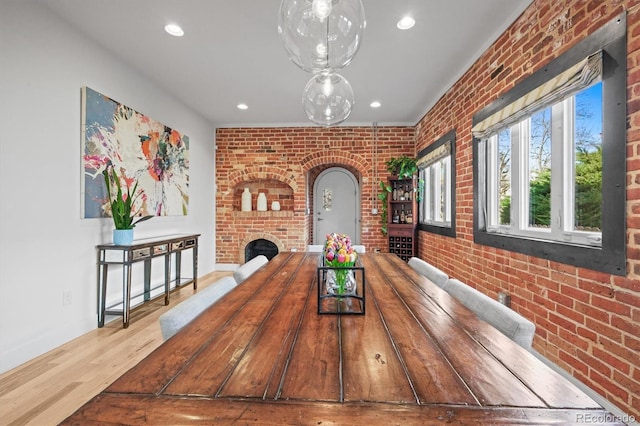 dining space with a brick fireplace, brick wall, recessed lighting, wood finished floors, and arched walkways