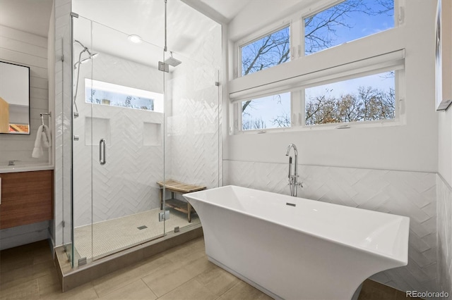 bathroom with tile walls, a shower stall, a freestanding bath, and vanity