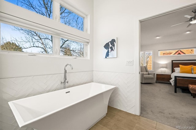 ensuite bathroom with a ceiling fan, a wainscoted wall, ensuite bath, a soaking tub, and tile walls