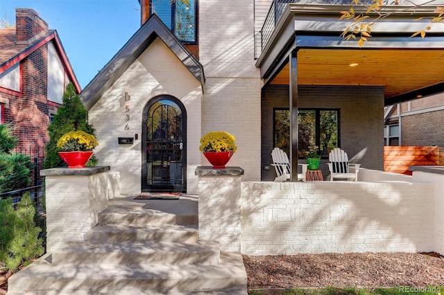 view of exterior entry with fence and brick siding