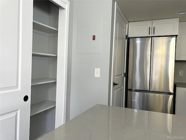 kitchen with electric panel, white cabinetry, and stainless steel refrigerator