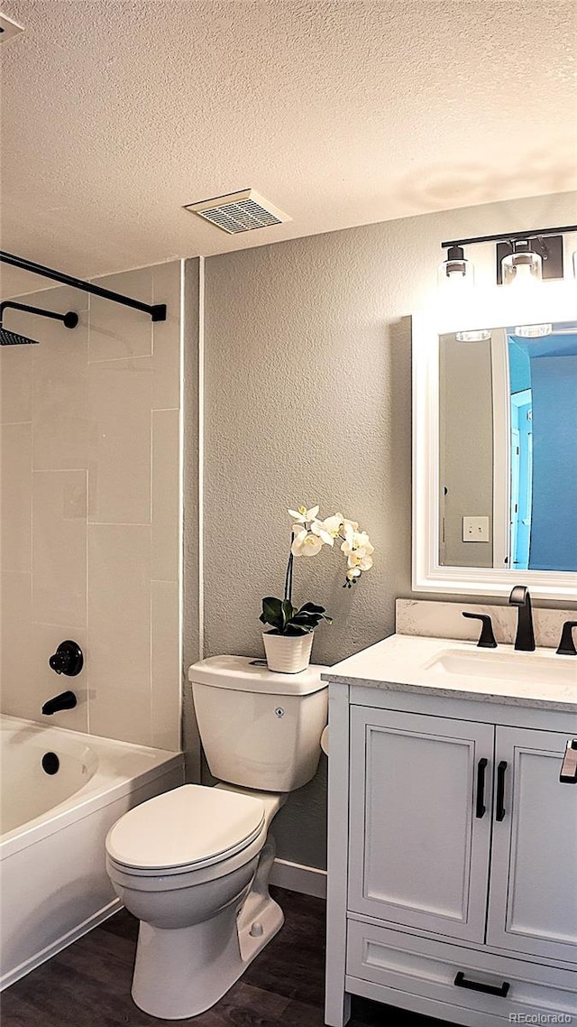 full bathroom with tiled shower / bath combo, wood-type flooring, a textured ceiling, toilet, and vanity