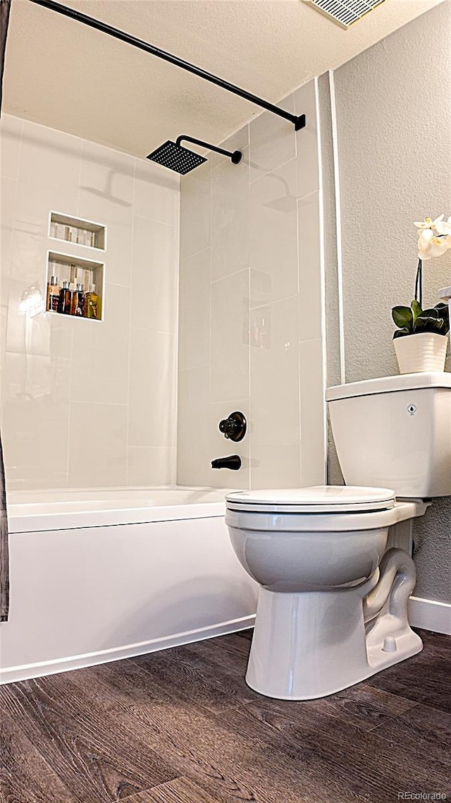 bathroom with hardwood / wood-style flooring, tiled shower / bath, a textured ceiling, and toilet