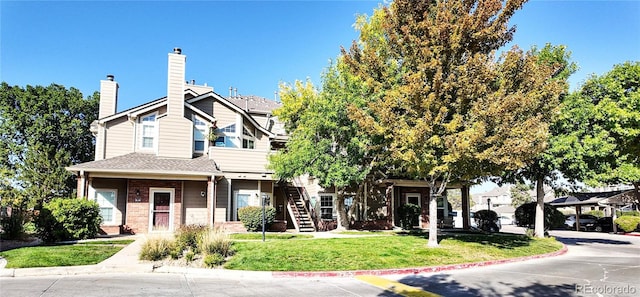 view of property with stairs, a front yard, a chimney, and brick siding