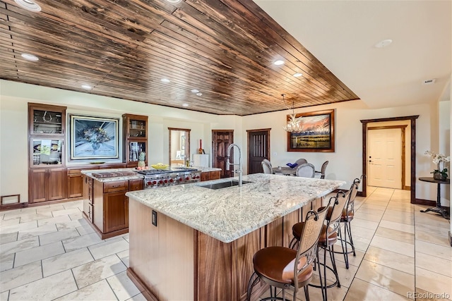 kitchen with wood ceiling, an island with sink, light stone countertops, sink, and decorative light fixtures