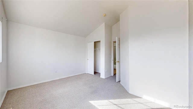 unfurnished bedroom featuring baseboards, vaulted ceiling, a closet, and light colored carpet