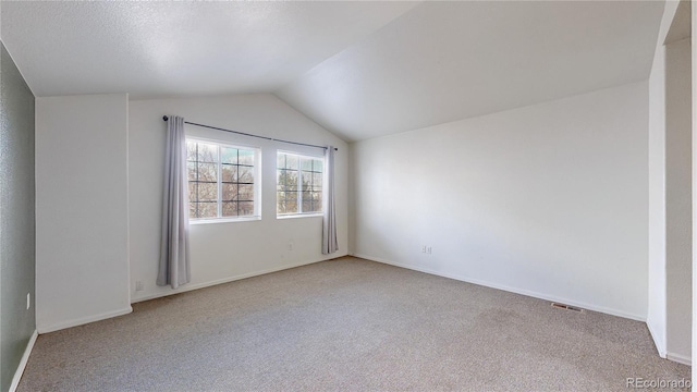 empty room featuring lofted ceiling, light carpet, visible vents, and baseboards