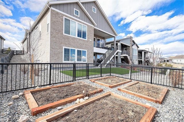 rear view of property featuring a fenced backyard, a vegetable garden, board and batten siding, and brick siding