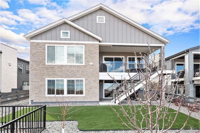 back of property with stairway, fence, a yard, board and batten siding, and brick siding