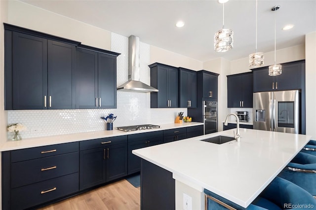 kitchen with a breakfast bar area, stainless steel appliances, a sink, wall chimney exhaust hood, and decorative light fixtures