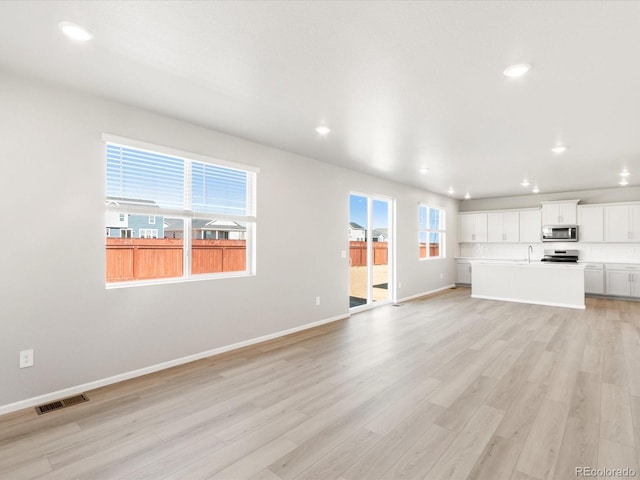 unfurnished living room featuring visible vents, baseboards, a healthy amount of sunlight, and light wood finished floors