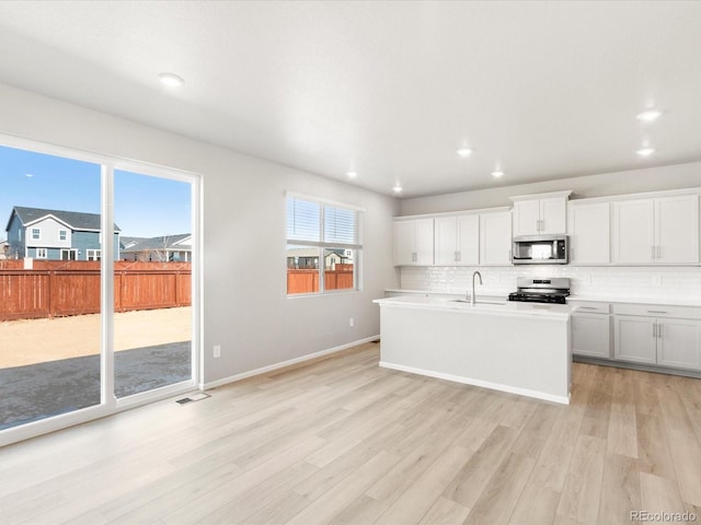 kitchen with a kitchen island with sink, light wood finished floors, tasteful backsplash, and appliances with stainless steel finishes